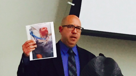 Detective Michael Berbiar holding a photo of a smiling Kirk Doffing at the West Hollywood Public Safety Commission meeting