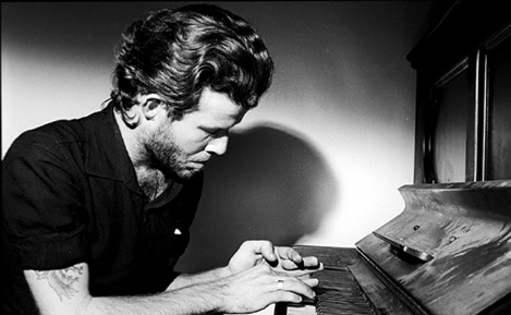 This 1977 photo shows Tom Waits playing piano in his Tropicana room. Waits supposedly “enlarged” the doorframe in order to get the piano inside. (Photo by Mitchell Rose)